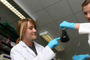 Das Bild zeigt zwei Studierende im Labor, die gerade eine Flüssigkeit in einem Becherglas untersuchen.